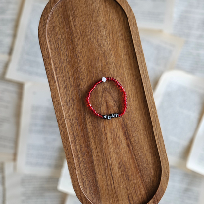 Red bracelet with black beads on a wooden tray