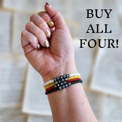 Hand wearing four bracelets with book titles against a blurred background