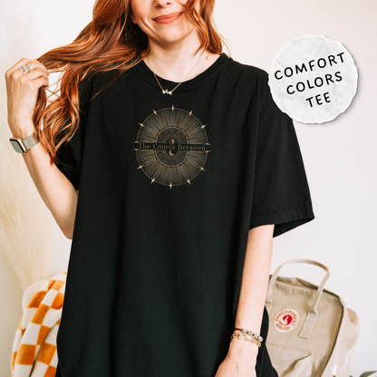 A woman wearing an oversized black t-shirt with a celestial design and the words "The Courts Between". is printed across the center of the design.