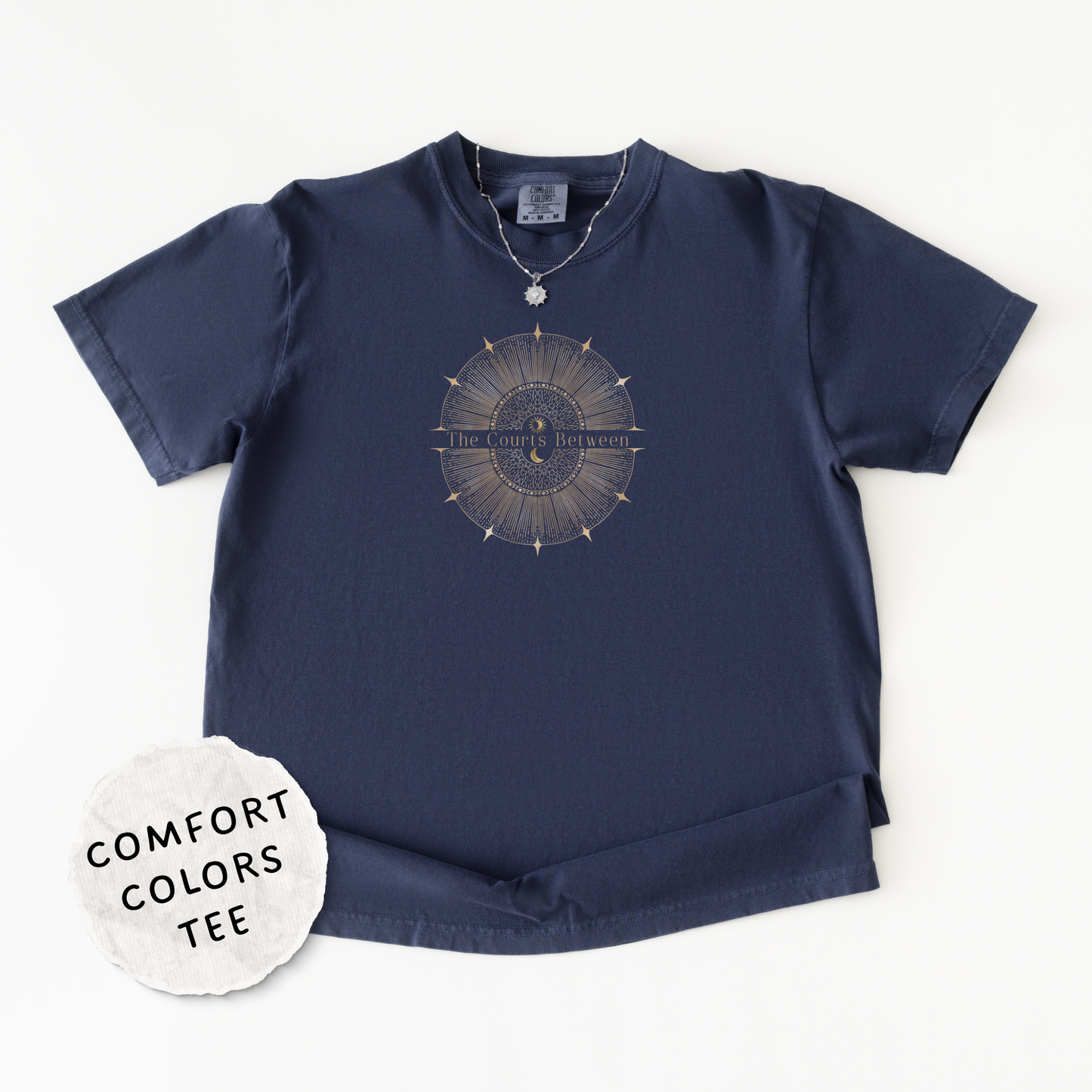 A navy blue Comfort Colors short-sleeve t-shirt with a celestial design and the words "The Courts Between". is printed across the center of the design with a 'COMFORT COLORS TEE' label sticker overlay.