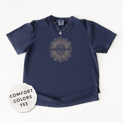 A navy blue Comfort Colors short-sleeve t-shirt with a celestial design and the words "The Courts Between". is printed across the center of the design with a 'COMFORT COLORS TEE' label sticker overlay.