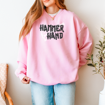 Person wearing a pink sweatshirt with 'HAMMER HAND' text and graphic, standing indoors.