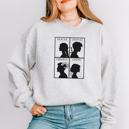A woman wearing a light gray heather crewneck sweatshirt with a black graphic print on the front showing four silhouettes and the words 'RESCUE', 'DEFEND', 'OBSERVE', and 'UNITE'.