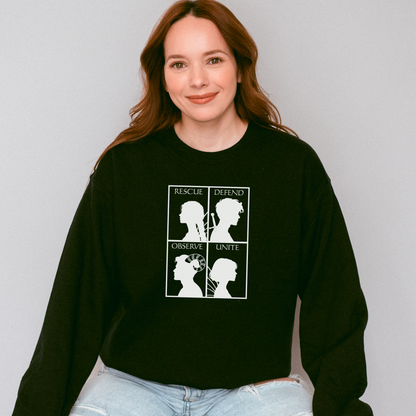 A woman with long red-brown hair wearing a black crewneck sweatshirt with a white graphic print of four silhouettes and the words 'RESCUE', 'DEFEND', 'OBSERVE', and 'UNITE'. She is wearing light-wash blue jeans against a plain light gray background.