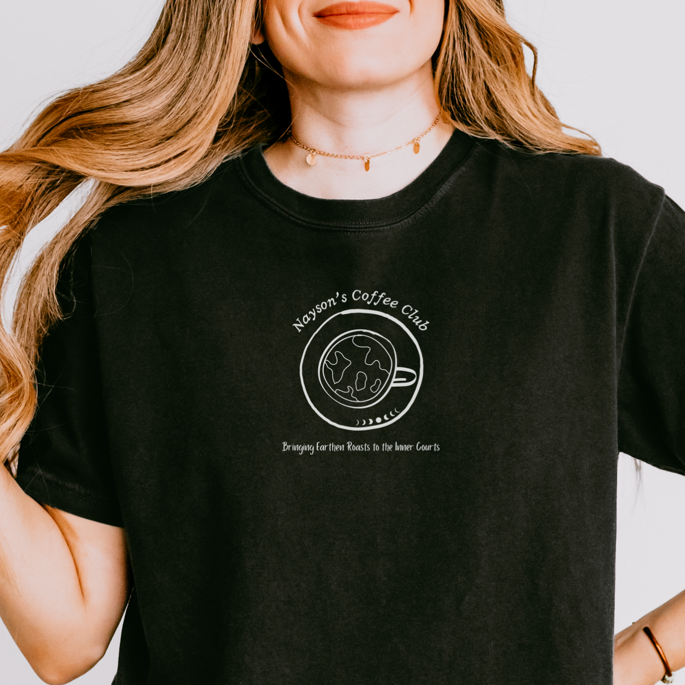 A woman wearing a black graphic t-shirt with a white line art design of a coffee cup and the words 'Nayson's Coffee Club'.