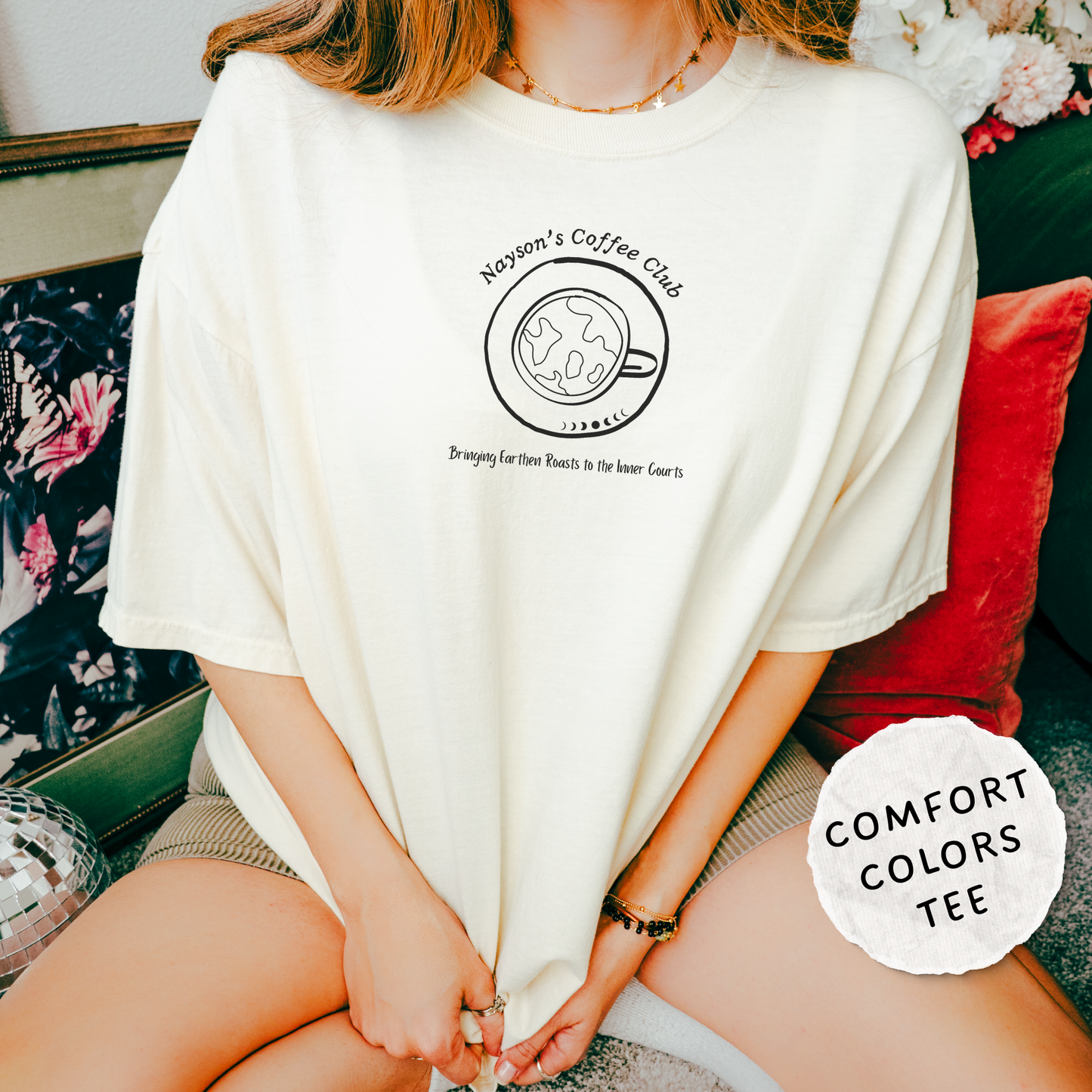 A person wearing an oversized cream-colored t-shirt with a black graphic that reads 'Nayson's Coffee Club'. A white circular badge in the bottom right corner reads 'COMFORT COLORS TEE'.
