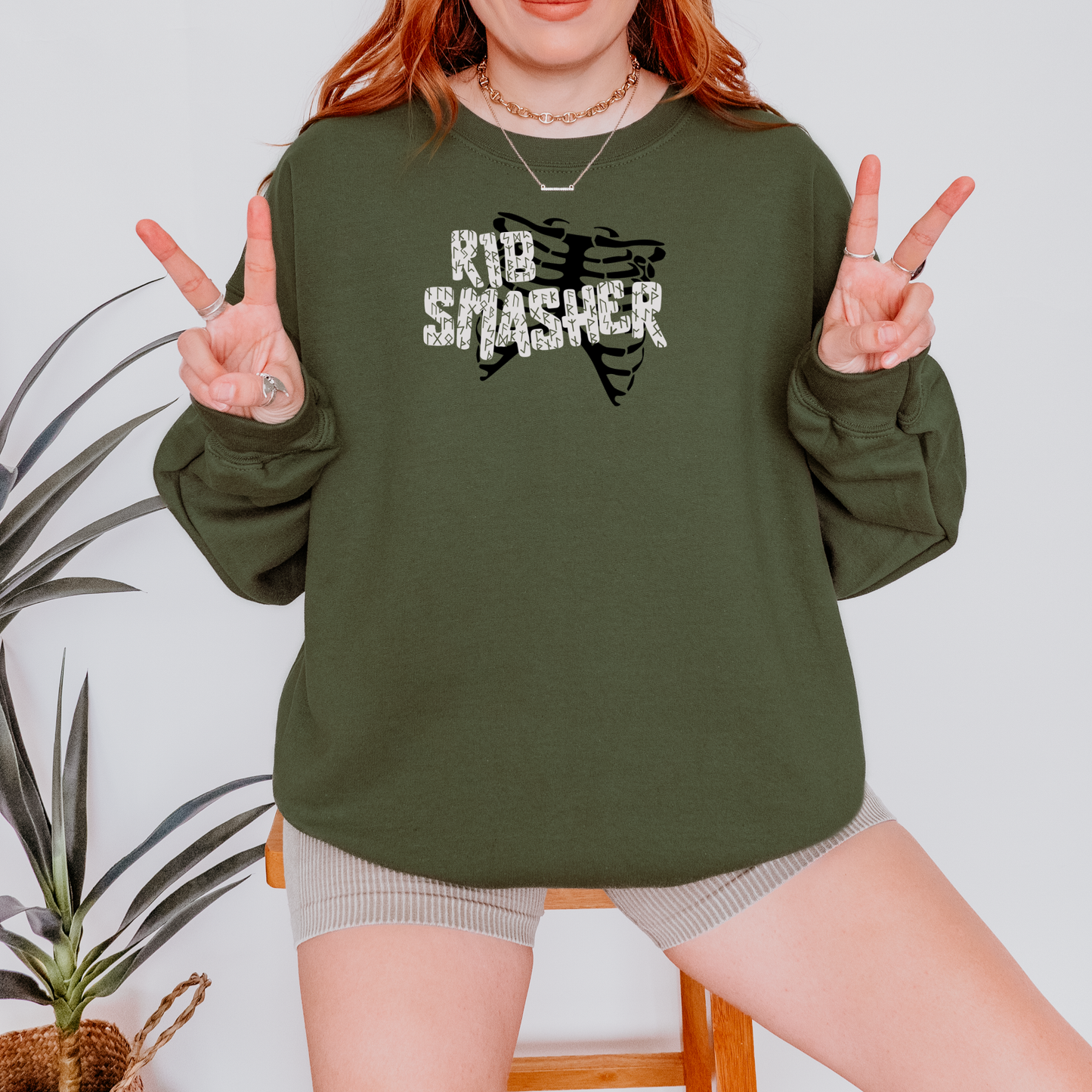 Person wearing a green sweatshirt with 'KID SMASHER' text, making peace signs.