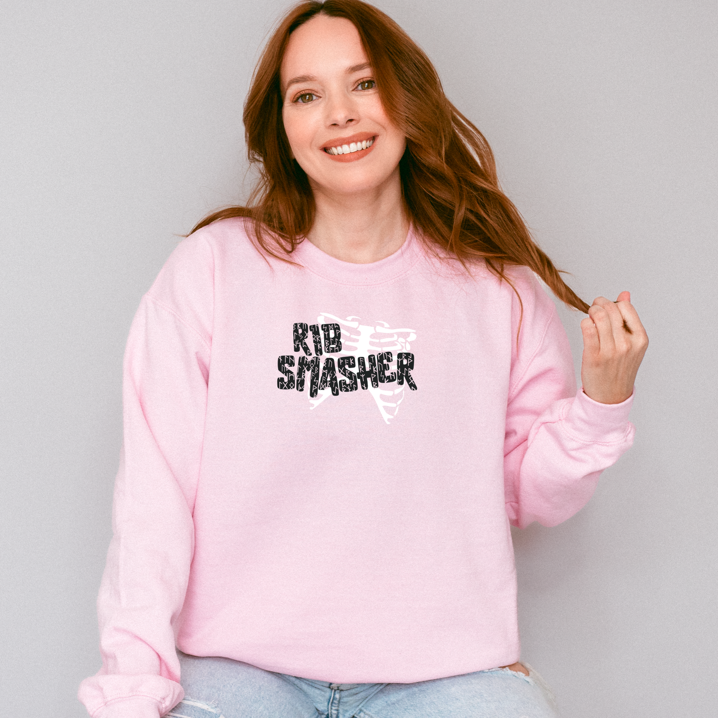 Woman wearing a pink sweatshirt with 'KID SMASHER' text, standing against a plain background